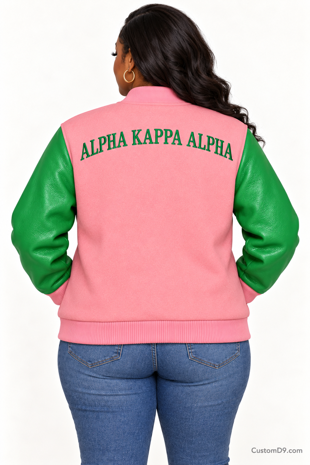 Black woman modeling Alpha Kappa Alpha salmon pink body and apple green sleeve premium varsity jacket, back view; arched organization name across upper back.