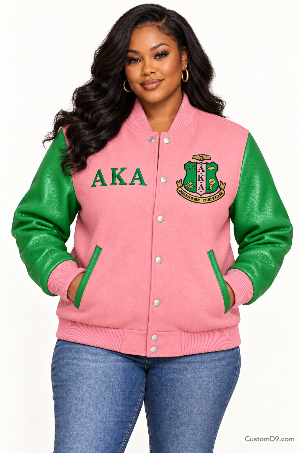 Black woman modeling Alpha Kappa Alpha salmon pink body and apple green sleeve premium varsity jacket, front view; horizontal Greek letters on right chest and crest on left chest.