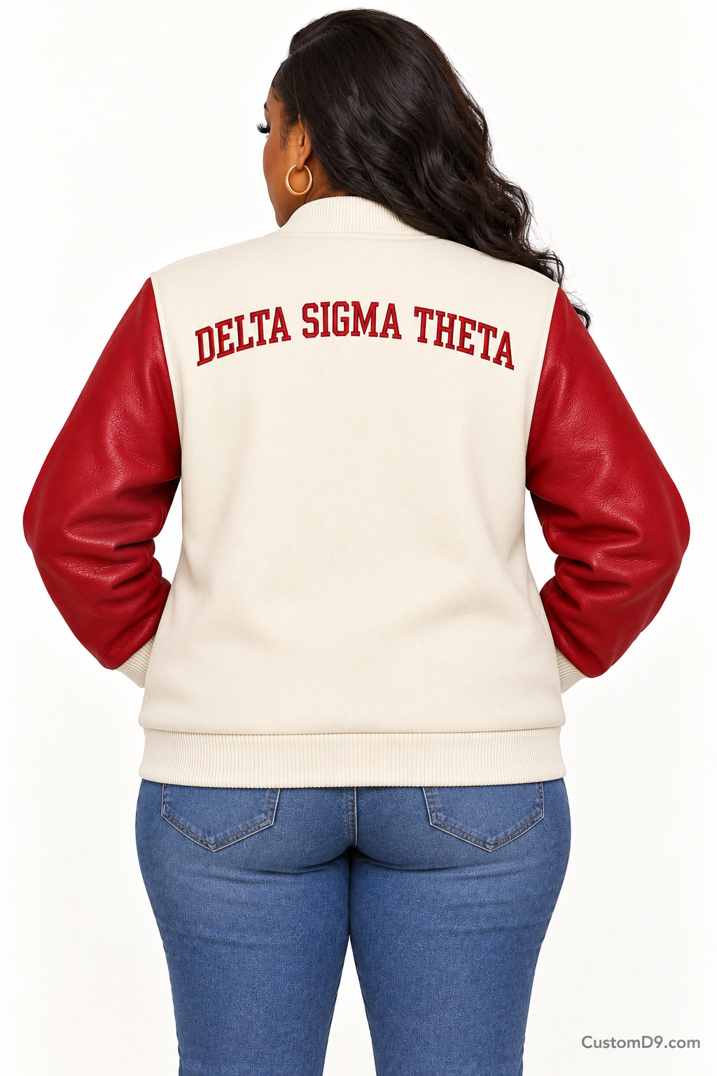 Black woman modeling Delta Sigma Theta cream body and crimson sleeve premium varsity jacket, back view; arched organization name across upper back.