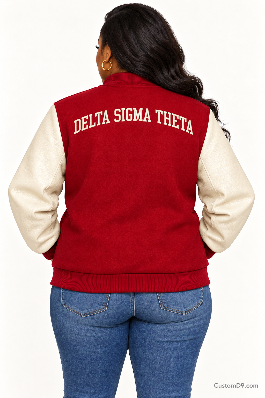 Black woman modeling Delta Sigma Theta crimson body and cream sleeve premium varsity jacket, back view; arched organization name across upper back.