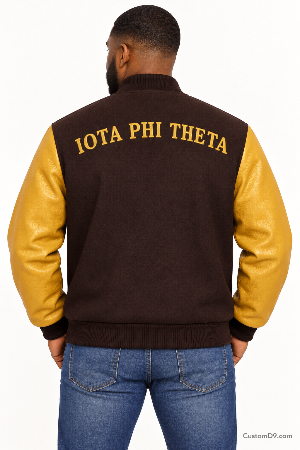 Black man modeling Iota Phi Theta premium contrast varsity jacket with charcoal brown body and gilded gold sleeves, back view.