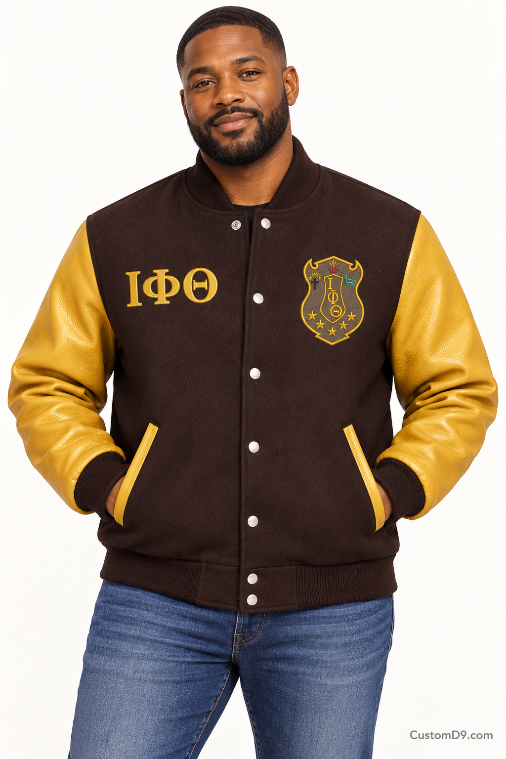 Black man modeling Iota Phi Theta premium contrast varsity jacket with charcoal brown body and gilded gold sleeves, front view.