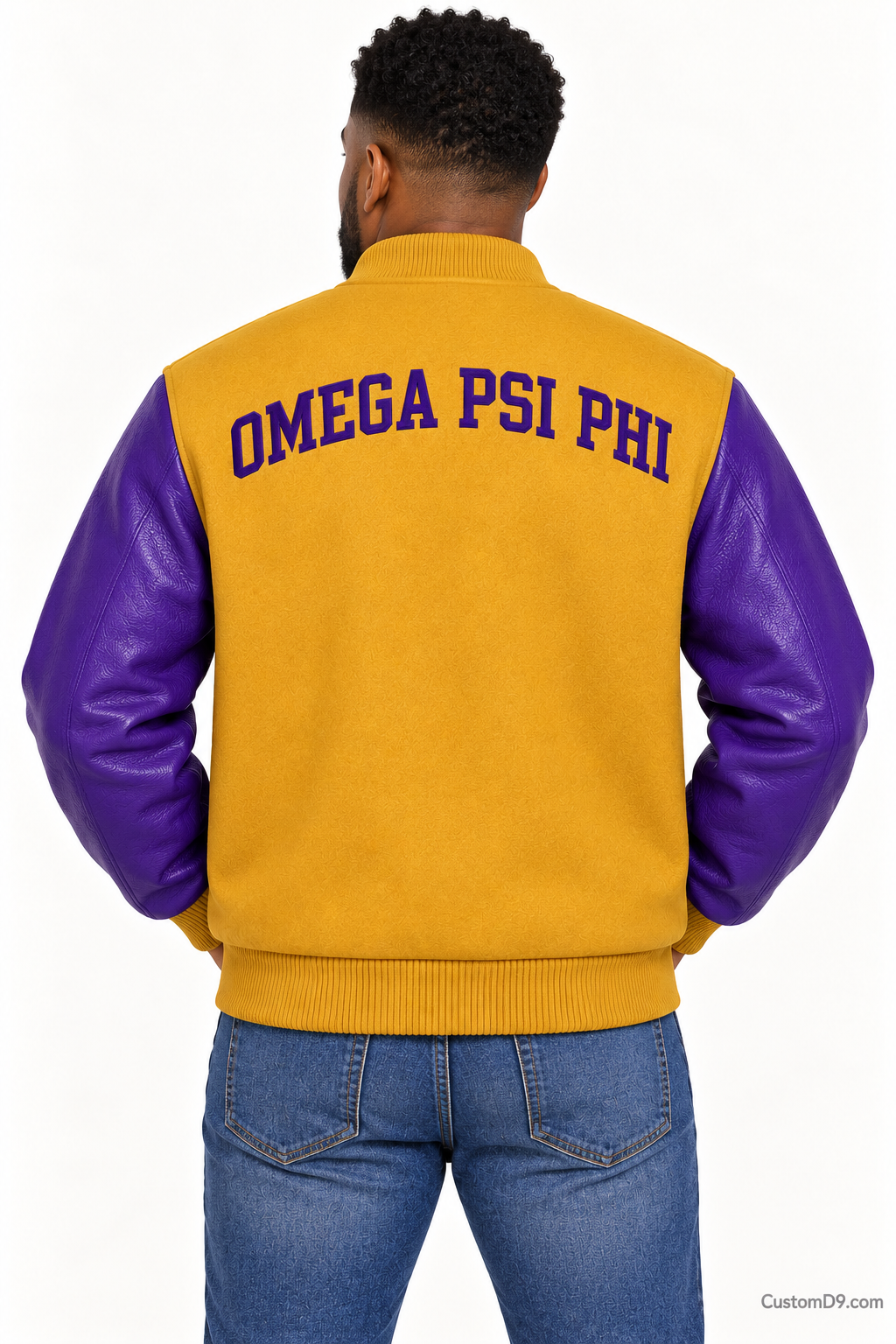 Black man modeling Omega Psi Phi premium contrast varsity jacket with old gold body and royal purple sleeves, back view.