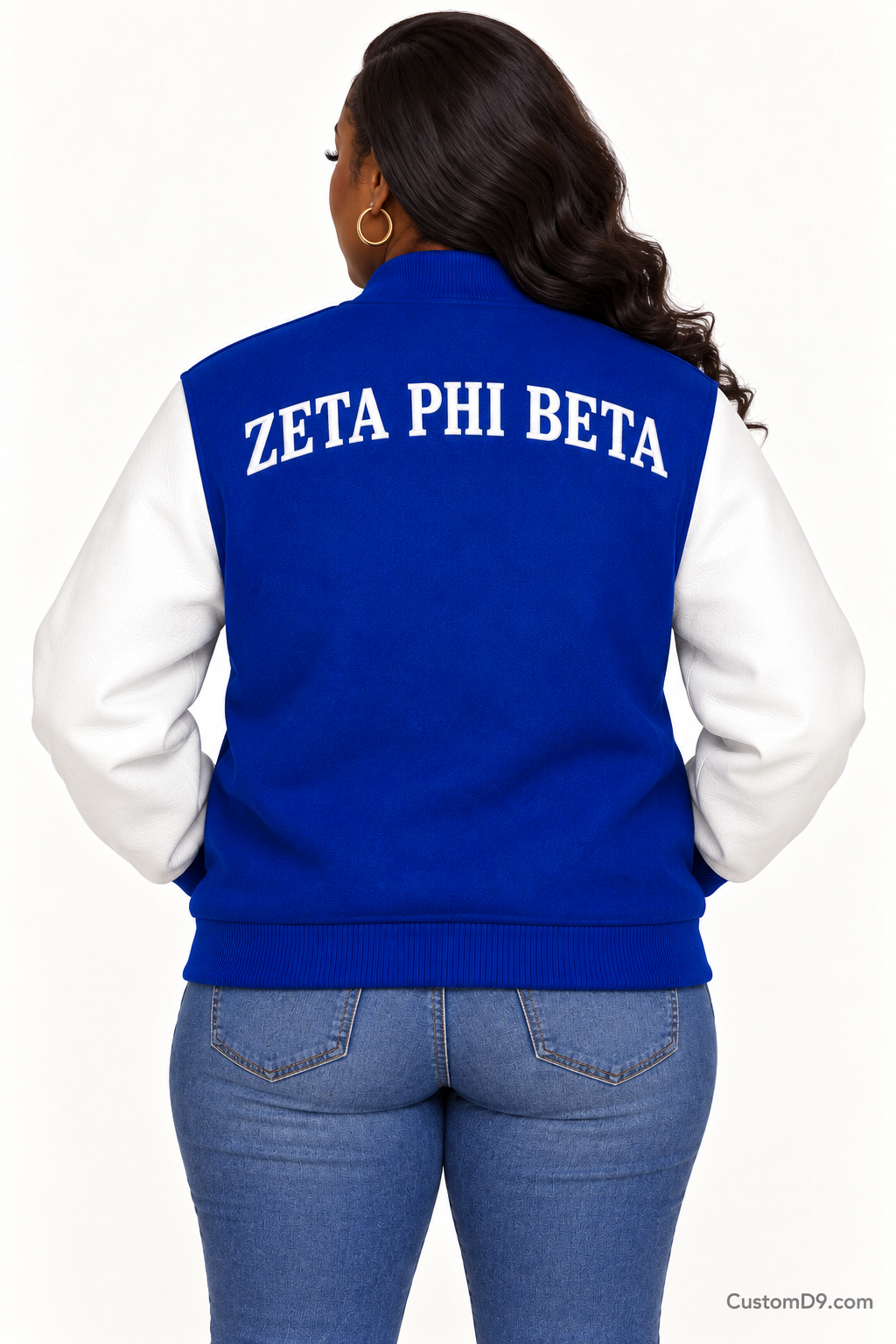 Black woman modeling Zeta Phi Beta royal blue body and white sleeve premium varsity jacket, back view; arched organization name across upper back.